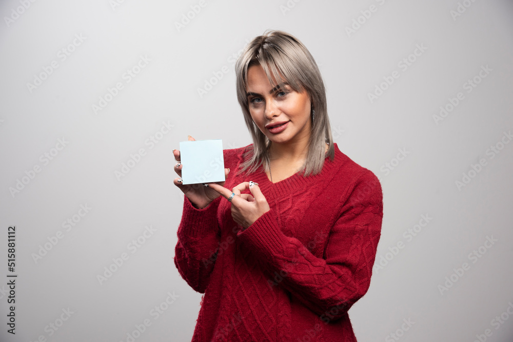 Woman pointing at memo pad on gray background Woman pointing at memo pad on gray background