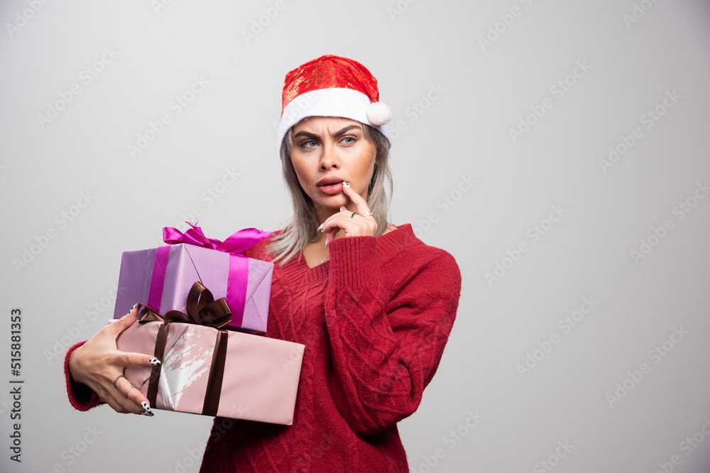 Serious looking woman in Santa hat holding Christmas gifts Serious looking woman in Santa hat holding Christmas gifts