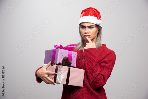 Serious looking woman in Santa hat holding Christmas gifts