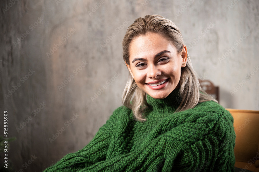 Smiling woman in green warm sweater sitting on the chair and posing Smiling woman in green warm sweater sitting on the chair and posing