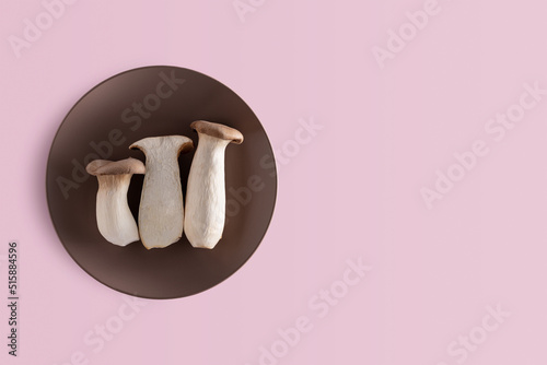 three Pleurotus eryngii in brown plate on pink background