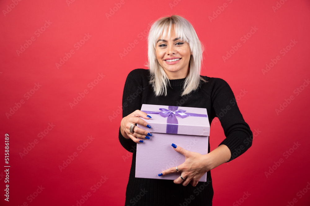 Young woman holding a present on a red background Young woman holding a present on a red background