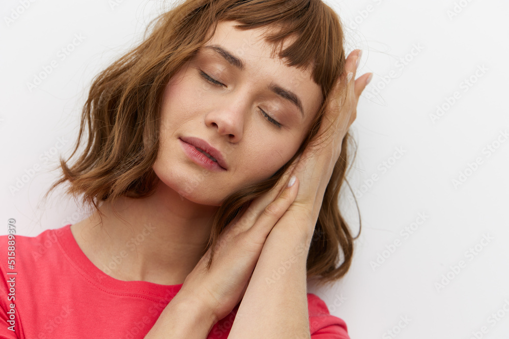 a gentle, relaxed, sleepy woman stands in a red T-shirt on a white background and holds her hands folded in her palms under her head, closing her eyes a gentle, relaxed, sleepy woman stands in a red T-shirt on a white background and holds her hands folded in her palms under her head, closing her eyes
