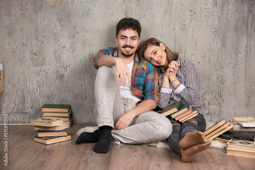 Photo of young smiling couple sitting on the floor with books
