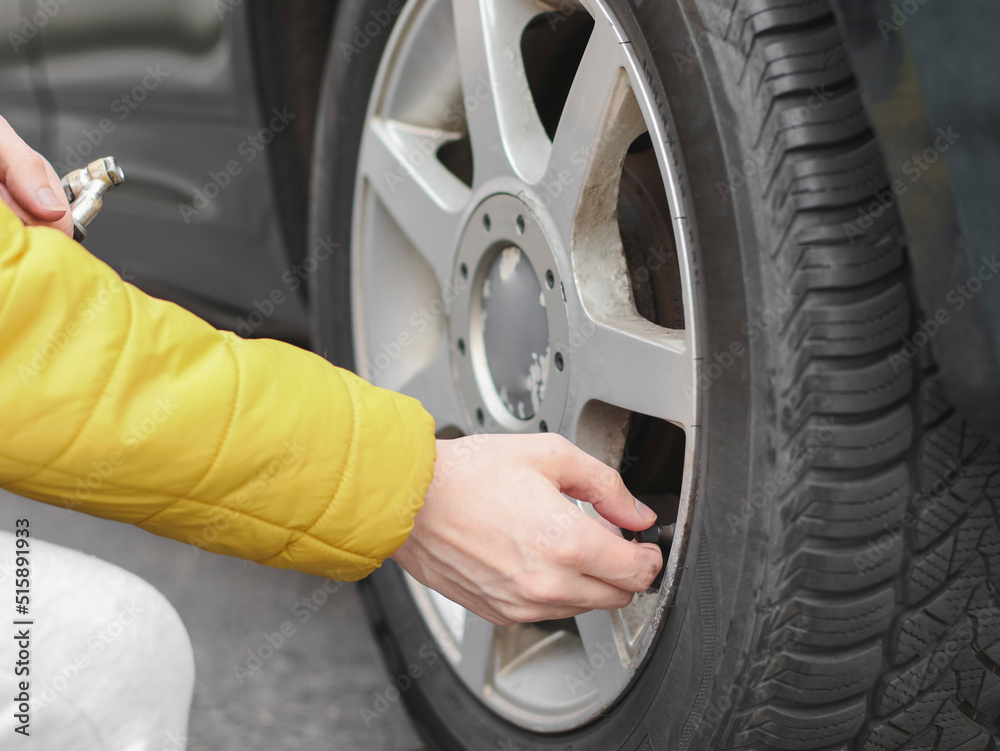 The hand of a young caucasian man in a yellow jacket winds the spool tip on the dirty rear wheel of a car The hand of a young caucasian man in a yellow jacket winds the spool tip on the dirty rear wheel of a car