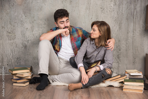 Photo of young couple sitting on the floor with books