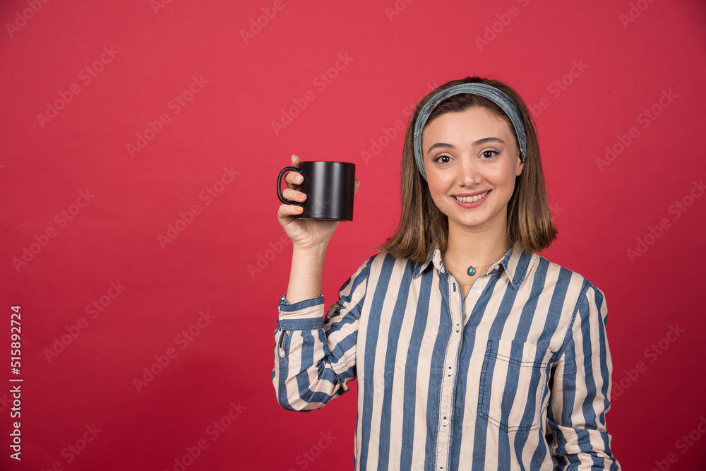 Cheerful woman showing cup of coffee and posing to camera Cheerful woman showing cup of coffee and posing to camera
