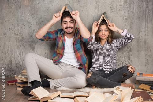 Image of funny couple sitting on the floor and holding books overhead