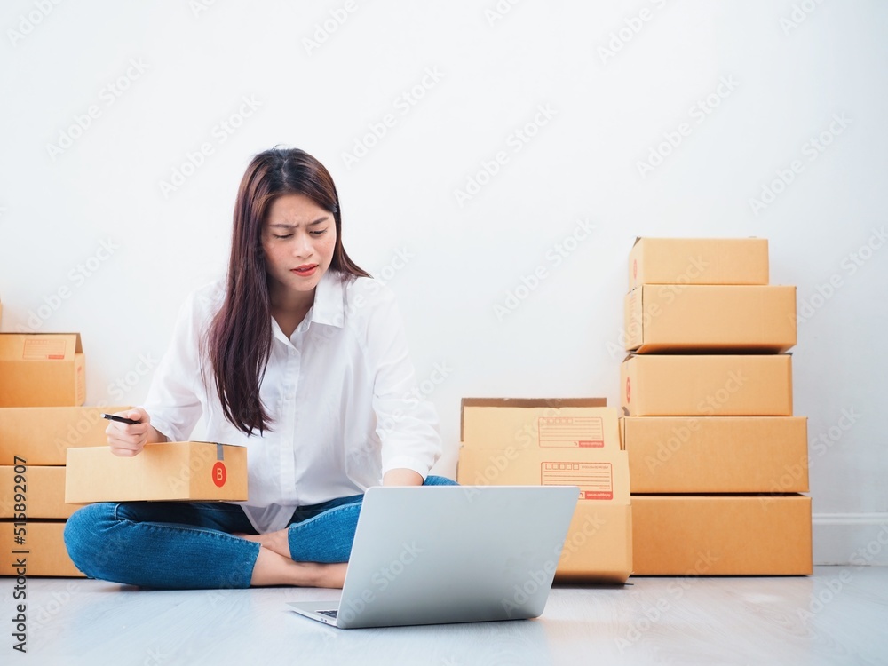 Upset Asian people checking order online on laptop,Asian woman packing parcel at home. Upset Asian people checking order online on laptop,Asian woman packing parcel at home.