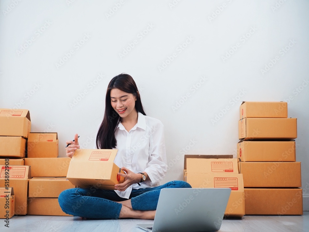 Cheerful Asian people checking order online on laptop,Asian woman packing parcel at home. Cheerful Asian people checking order online on laptop,Asian woman packing parcel at home.