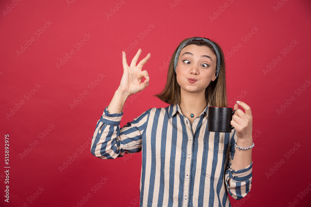 Young woman holding cup of coffee and giving ok sign Young woman holding cup of coffee and giving ok sign