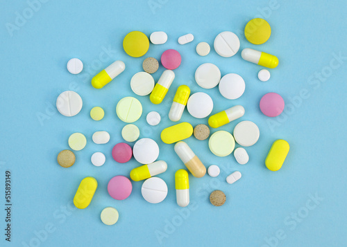 Pills of different sizes and colors on a blue background. Capsules and tablets colored top view. Dietary supplements of various types.
