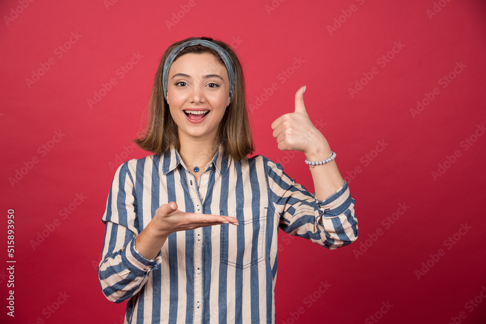Female teenager in striped shirt holding open space and giving thumbs up Female teenager in striped shirt holding open space and giving thumbs up
