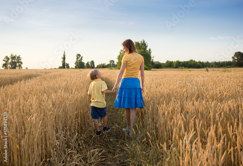 mother and son son in mother's arms walk holding hands among spikelets in a wheat field. Enjoy nature and life. Countryside, agriculture, farming. Earth Day. Harvest in Ukraine photo