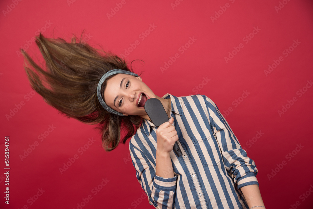 Young funny girl sings using black hairbrush on red background Young funny girl sings using black hairbrush on red background