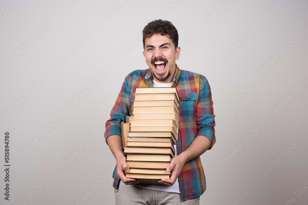 Exhausted student with pile of books screaming on gray background Exhausted student with pile of books screaming on gray background