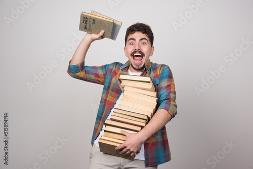 Joyful student trying to throw books over gray background