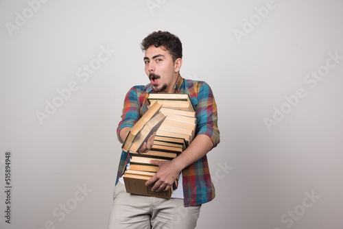 Young man holding heavy books on gray background