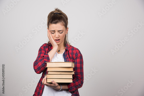 An upset woman looking at a stack of books on a gray wall