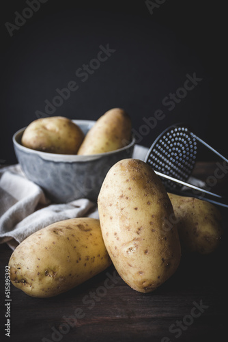 patatas crudas en una mesa y en un cuenco, con un prensa patatas para hacer puré