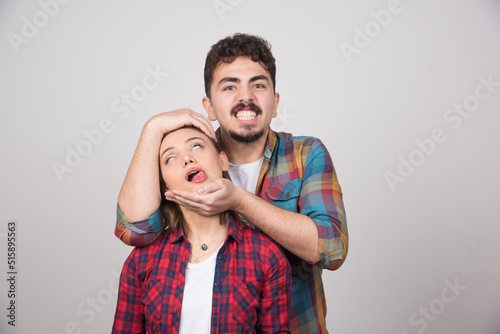 Fotografia Young man holding woman's head on a gray wall