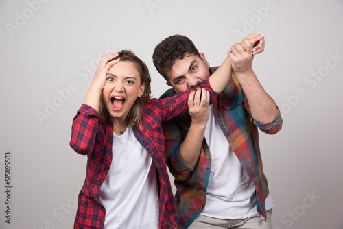 Young man trying to bite woman's hand on a gray wall
