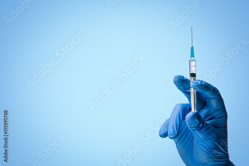 Doctors hand in surgical gloves holds a syringe on classic symbolic blue background photo