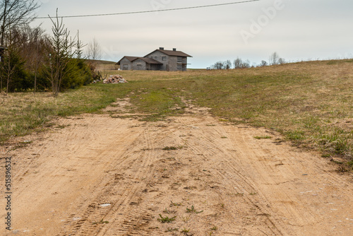 Summer landscape with country sandy road.in the distance the old wooden house.