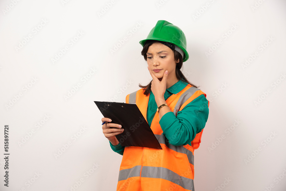 Thoughtful female industrial engineer in uniform with clipboard on white background Thoughtful female industrial engineer in uniform with clipboard on white background