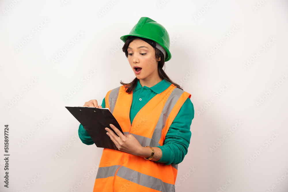 Fototapeta premium Shocked female industrial engineer in uniform with clipboard on white background