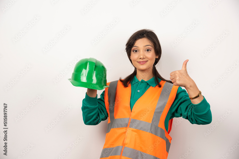 Female engineer showing thumb up and holding a helmet on white background Female engineer showing thumb up and holding a helmet on white background