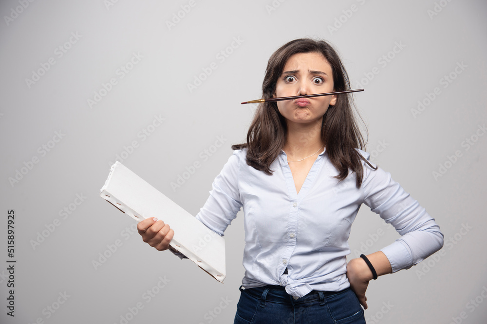 Tired woman playing with paintbrush over gray background Tired woman playing with paintbrush over gray background