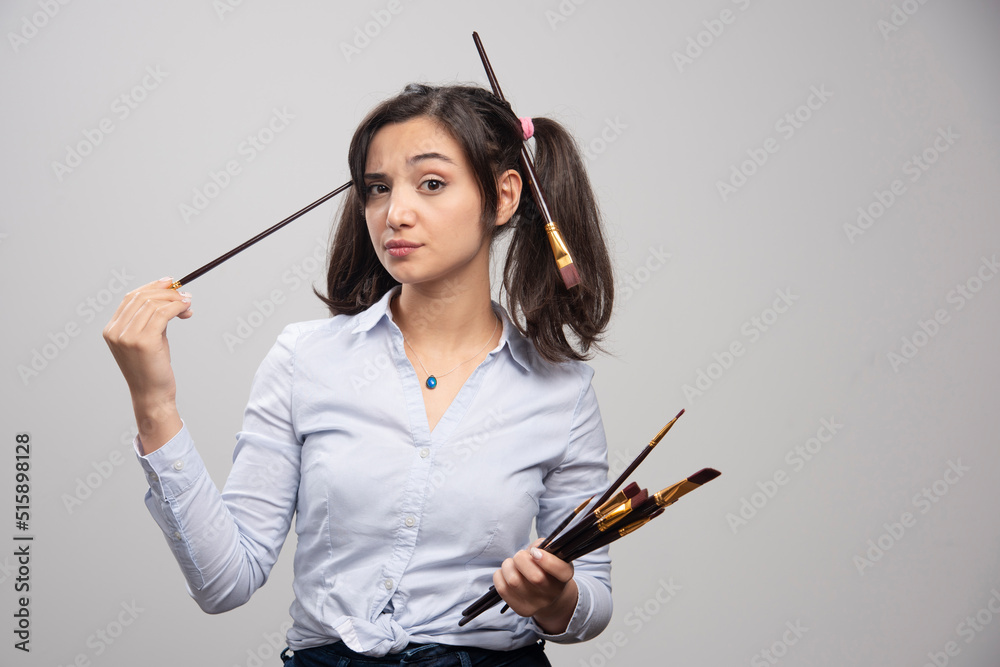 Young woman artist with paintbrushes posing on gray background Young woman artist with paintbrushes posing on gray background