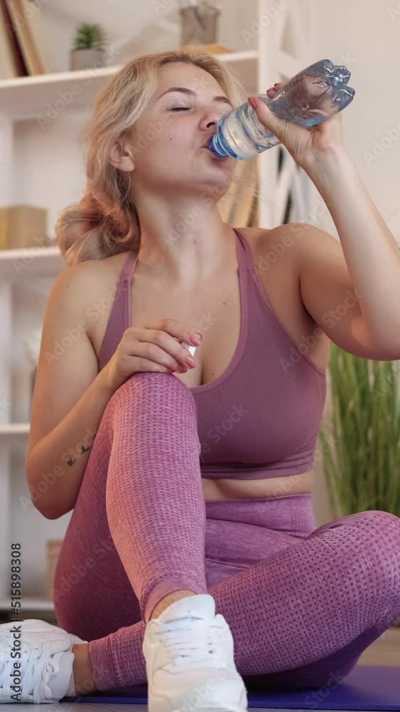 Vertical video. Water refreshment. Sporty woman. Healthy slimming. Joyful thirsty lady in sportswear drinking from bottle in light room interior. Vertical video. Water refreshment. Sporty woman. Healthy slimming. Joyful thirsty lady in sportswear drinking from bottle in light room interior.