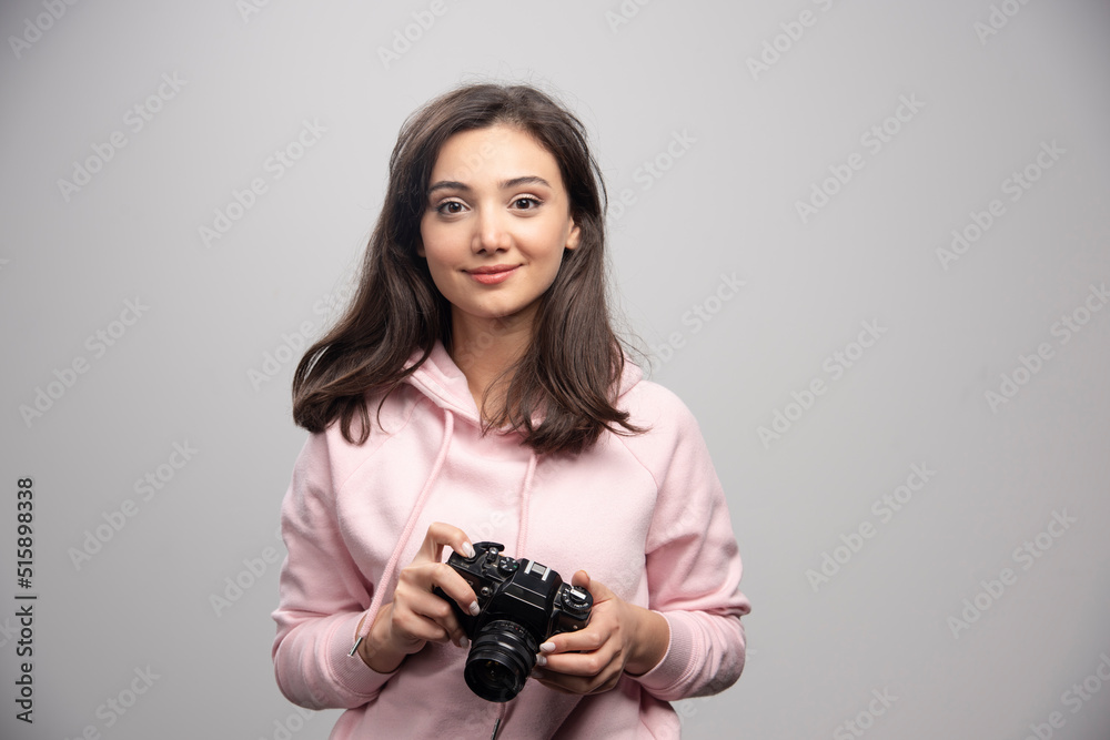 Pretty young woman standing with camera over a gray wall