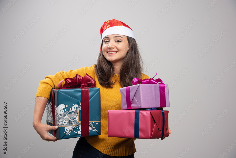 Young woman in Santa hat carrying Christmas presents Young woman in Santa hat carrying Christmas presents