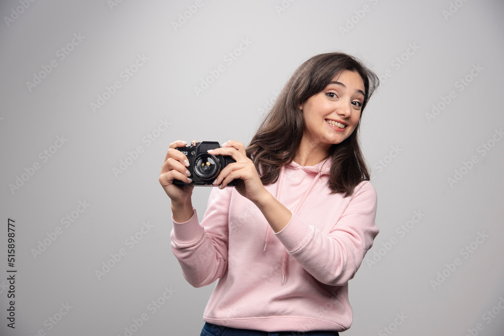 Pretty young woman posing with camera over a gray wall