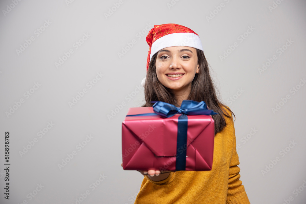 Smiling woman in Santa hat showing a gift box Smiling woman in Santa hat showing a gift box
