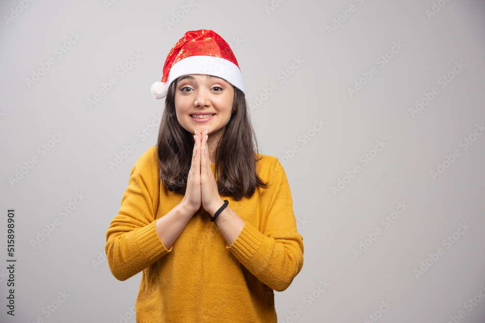 Young woman in Santa hat feeling grateful on gray background Young woman in Santa hat feeling grateful on gray background