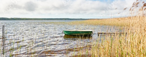 Small green boat anchored in forest lake. Scandinavia. Transportation, traditional craft, recreation, leisure activity, healthy lifestyle, local tourism, sport, rowing, hiking, summer vacations themes photo