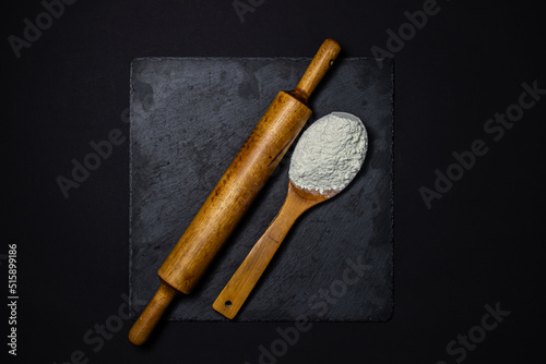 Wooden spoon with flour and a rolling pin on a black background. The concept of baking and confectionery.