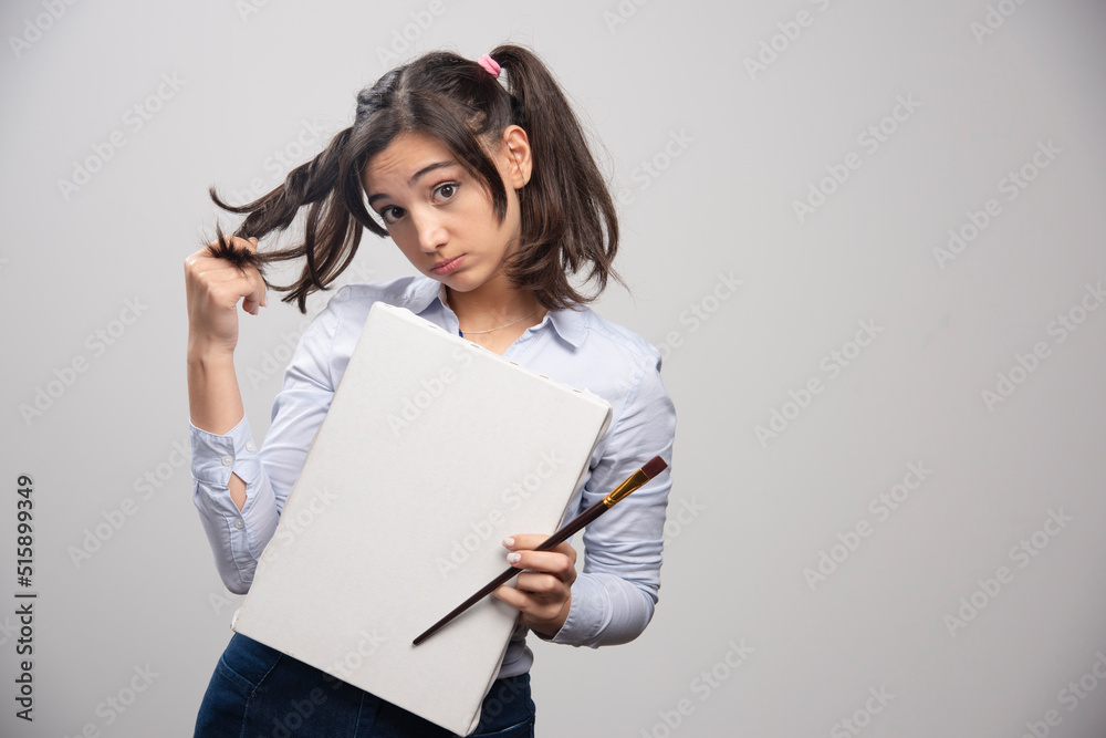 Young girl holding empty canvas and paintbrush on gray background Young girl holding empty canvas and paintbrush on gray background
