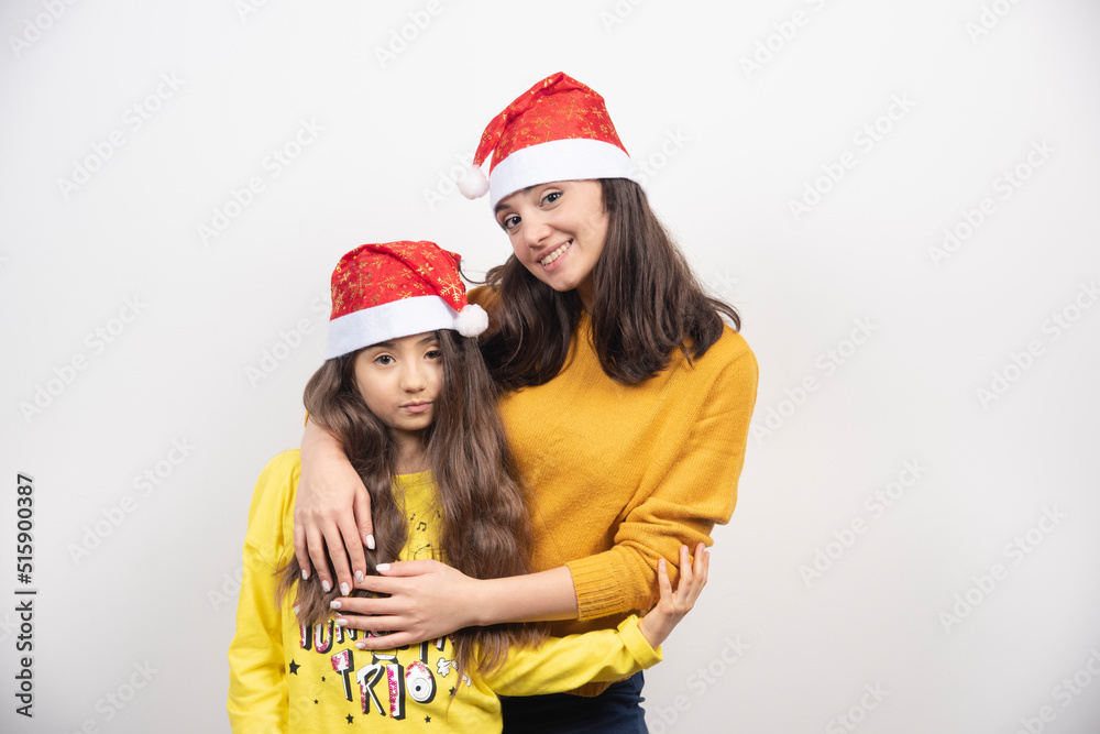 Woman hugging young girl with Santa Claus red hat Woman hugging young girl with Santa Claus red hat