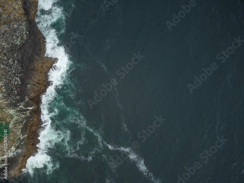Shooting from a drone. Dark blue calm surface of the ocean. Light white waves float on a rocky shore. Calm, calm scenes. The beauty and majesty of nature. Ecology, geology, marine tourism.