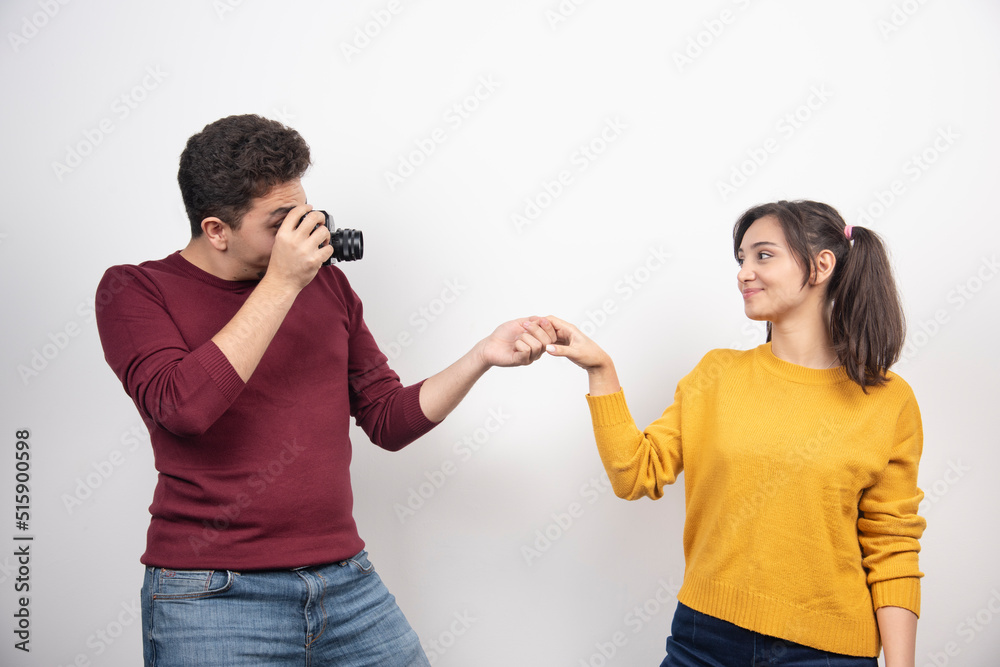 Cute couple taking pictures with camera and posing over a white wall Cute couple taking pictures with camera and posing over a white wall