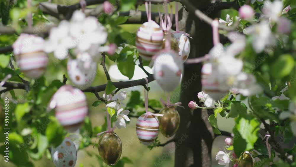 Decor eggs on flowering apple branches on a tree in a garden or park. Pink and gold ornament from stripes and spots.