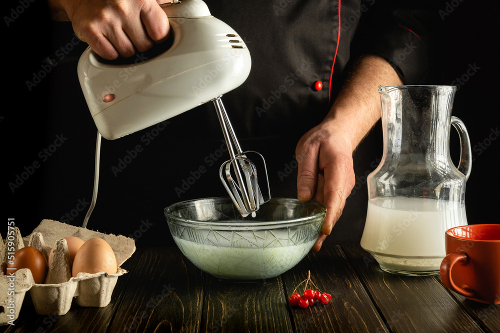 The chef prepares an egg omelette with milk using a hand-held electric mixer. Delicious breakfast or lunch in the kitchen. The chef prepares an egg omelette with milk using a hand-held electric mixer. Delicious breakfast or lunch in the kitchen.
