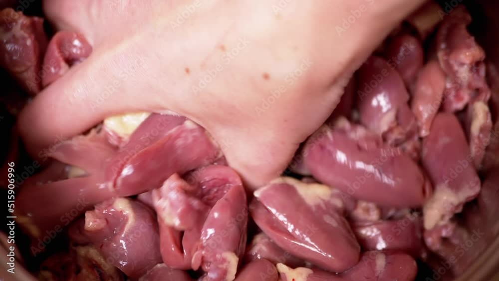 Female Hand Mixing Fresh Raw Peeled Chicken Hearts in a Plate. Close-up. Gutted shiny red chicken hearts, cut into two halves. Dietary meat. By-products of second grade. Cheap food for the poor.