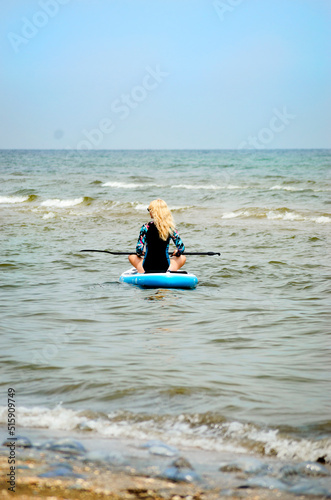 A blond woman in a wetsuit, engaged in snorkeling, sits on a board with an oar. © ketrin08