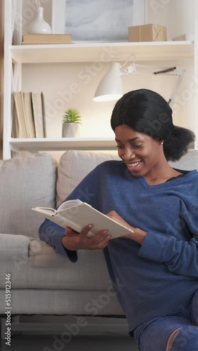 Vertical video. Reading joy. Happy woman. Home relax. Joyful lady enjoying book sitting floor light living room interior. photo
